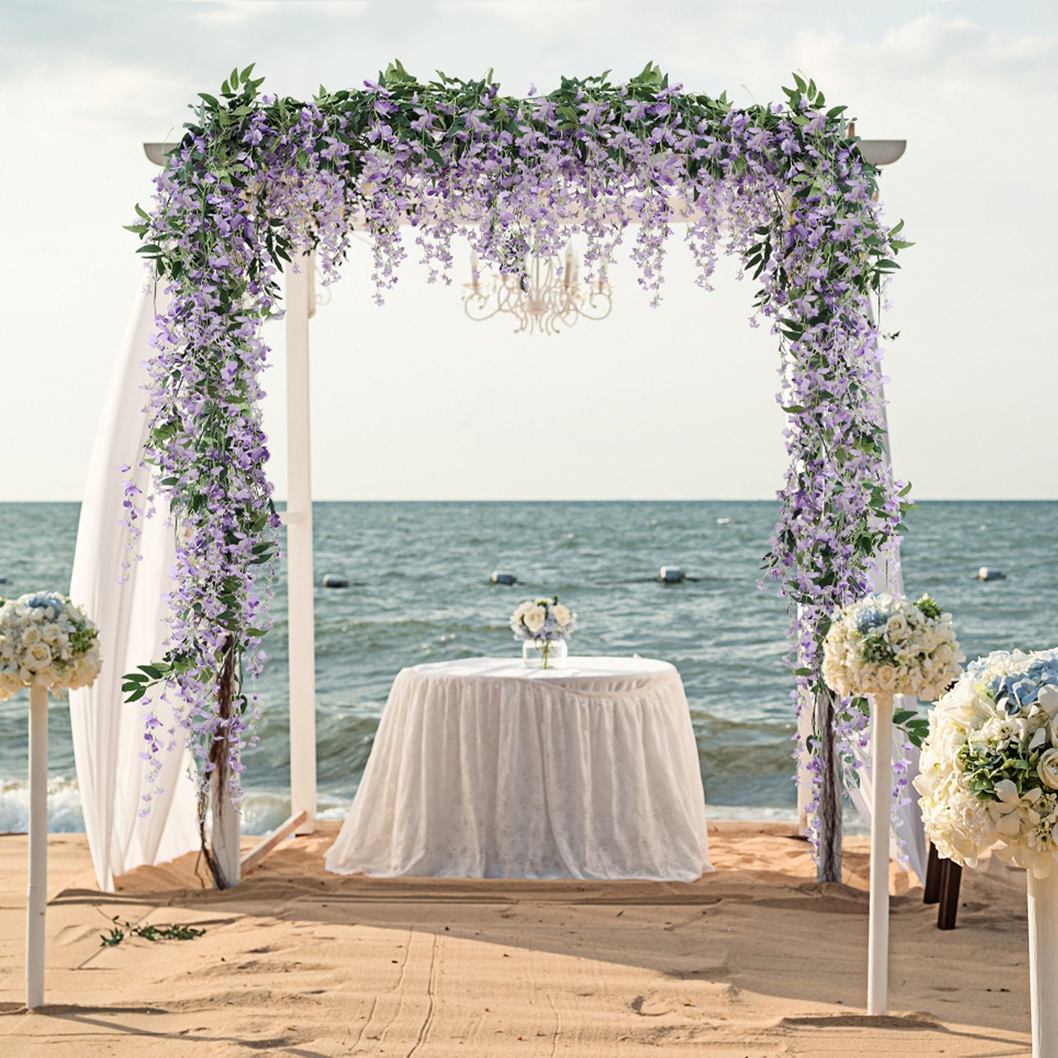 Wedding arch decorated with purple wisteria vines on a sandy beach with the ocean in the background.