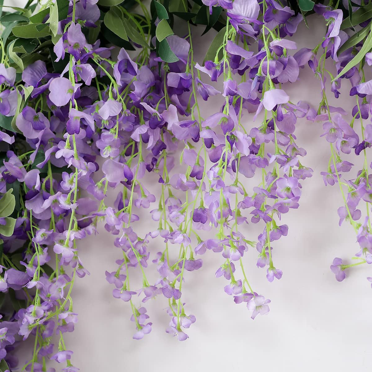 Artificial purple wisteria vine garland with green leaves cascading against a white background.