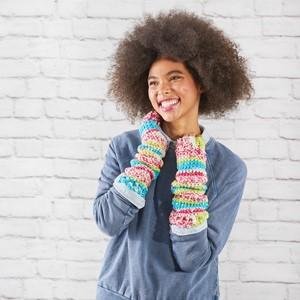 Woman with afro hairstyle wearing colorful striped arm warmers against a white brick wall