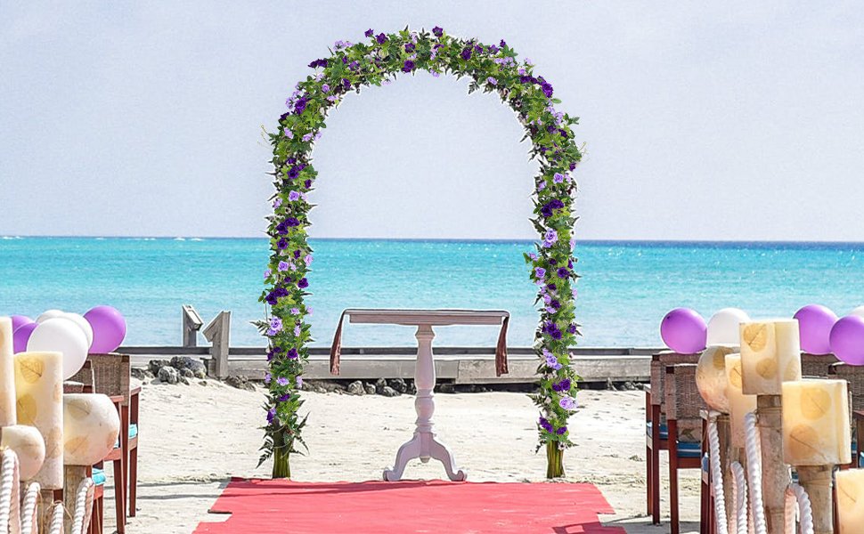 Wedding arch decorated with purple silk roses and green leaves on a beach with the ocean in the background.