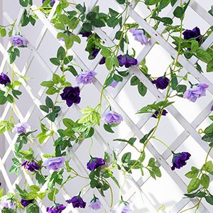 Artificial purple rose flower garland with green leaves draped on a white lattice trellis