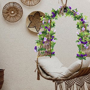 Artificial purple rose flower garland draped over a hanging chair, with green leaves and decorative wall hangings in the background.