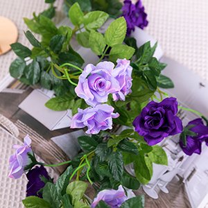 Artificial purple rose flower garland with green leaves draped on a textured surface.