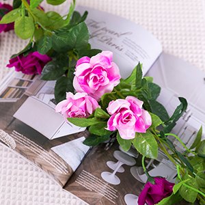 Artificial pink and purple rose flower garland with green leaves draped over an open magazine.