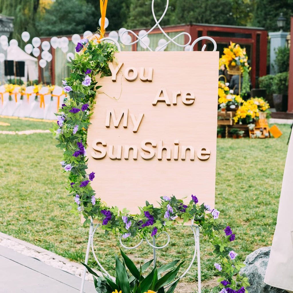 Artificial purple rose garland draped around a wooden sign that says 'You Are My Sunshine' at an outdoor event.