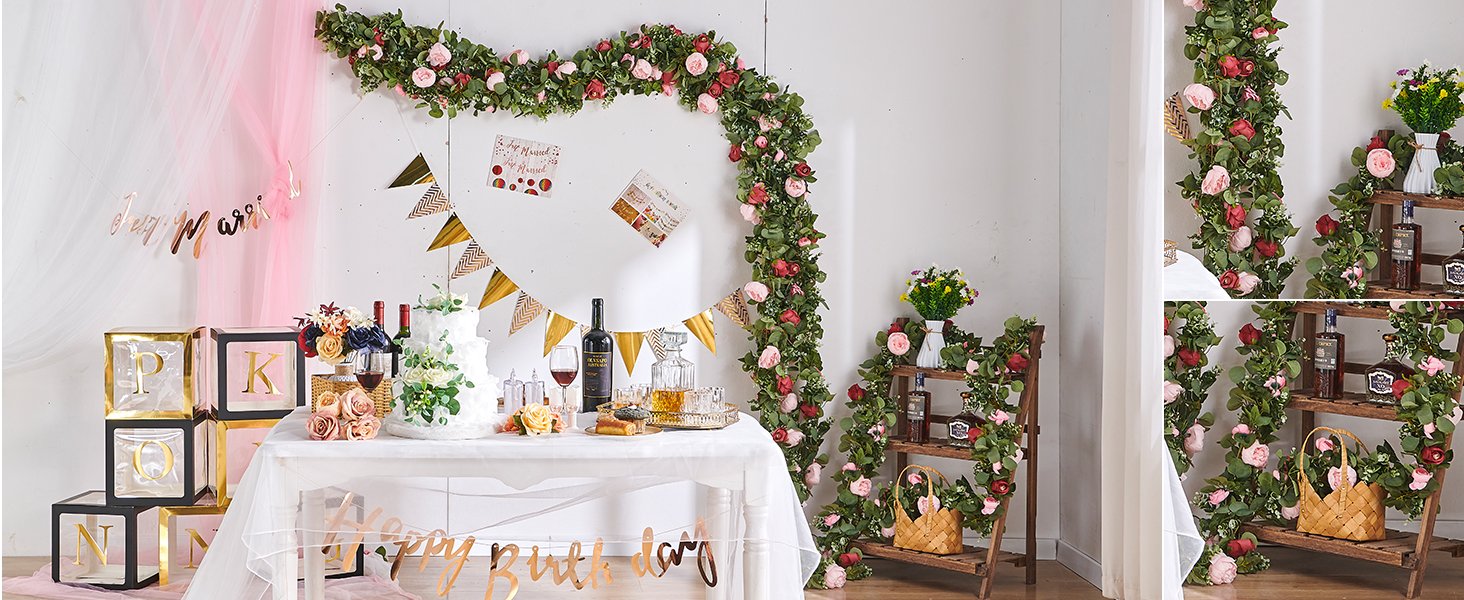 Artificial rose vine garlands draped around a party setting with a cake, wine, and decorative blocks.