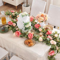 Artificial rose vine garland with off-white and dark pink silk flowers draped over a table with a cake and pastries.