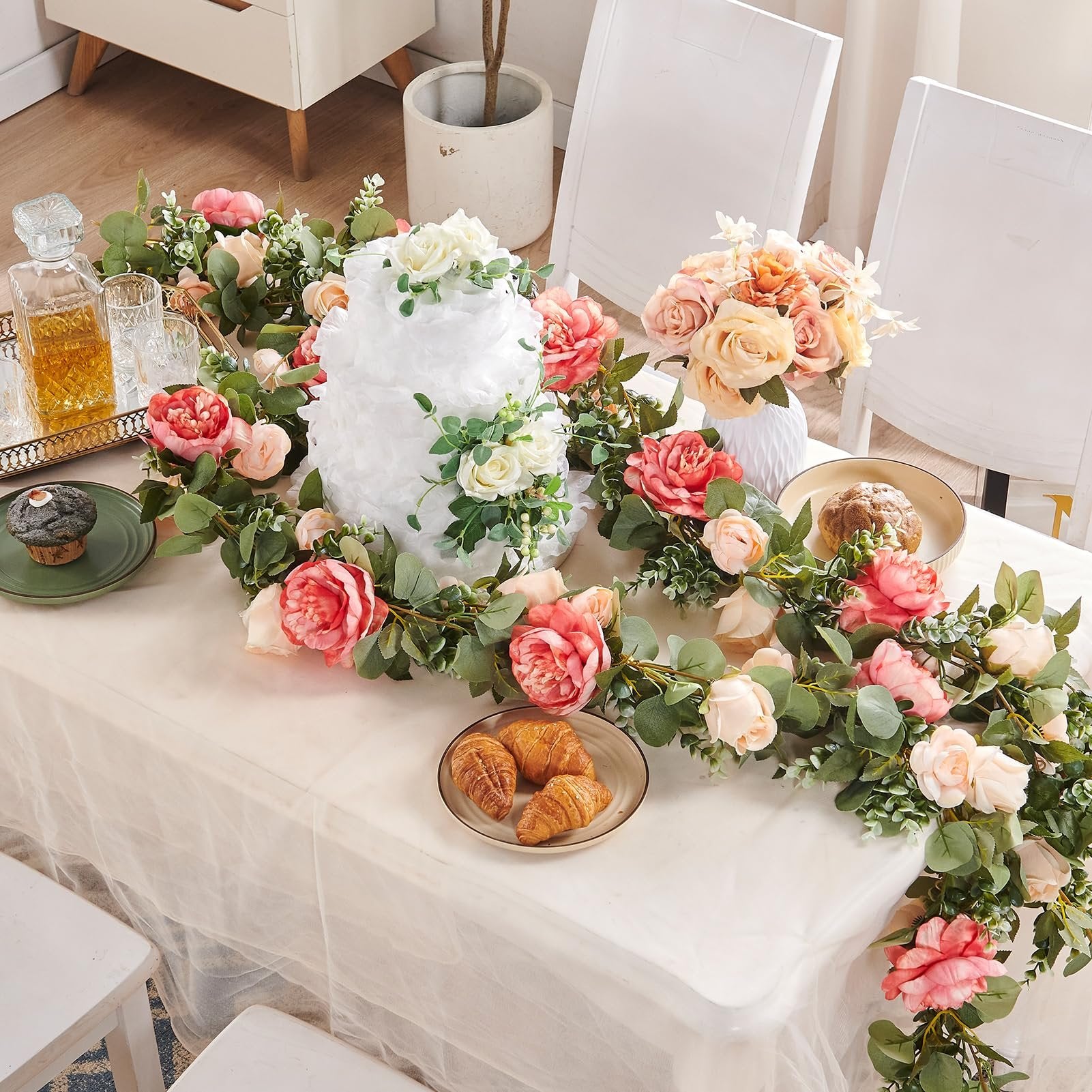 Artificial rose vine garland with off-white and dark pink silk flowers draped over a table with a cake and pastries.