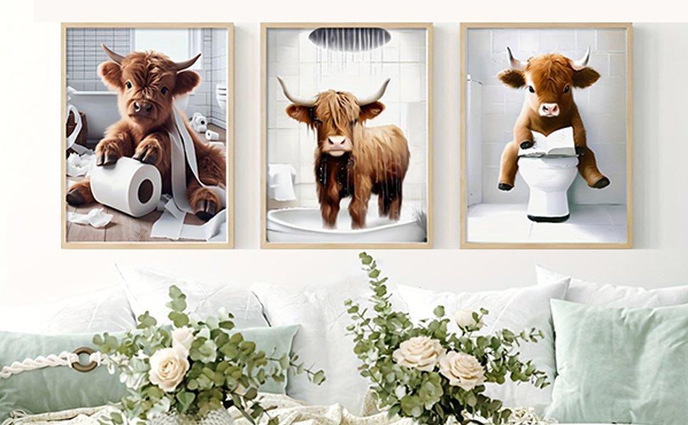 Three framed diamond art paintings of cows in bathroom scenes, displayed on a wall above pillows and flowers.