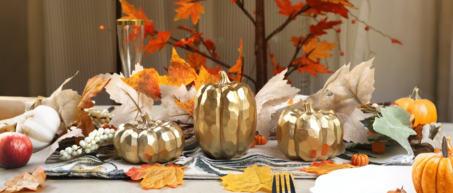 Three gold resin pumpkins arranged with fall leaves and decorative elements on a table.