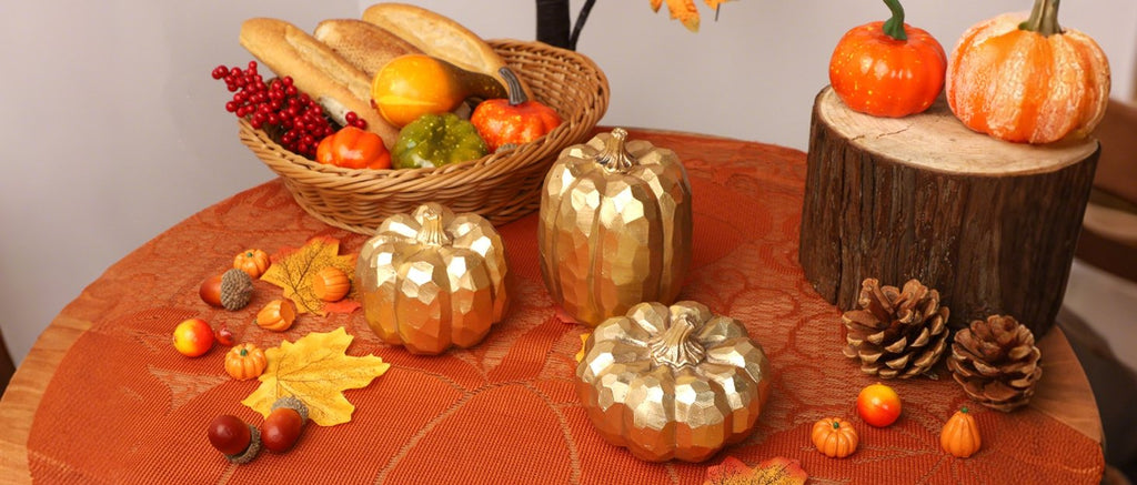 Three gold faceted pumpkins arranged on a table with fall decor, including a basket of bread and gourds, pinecones, and autumn leaves.