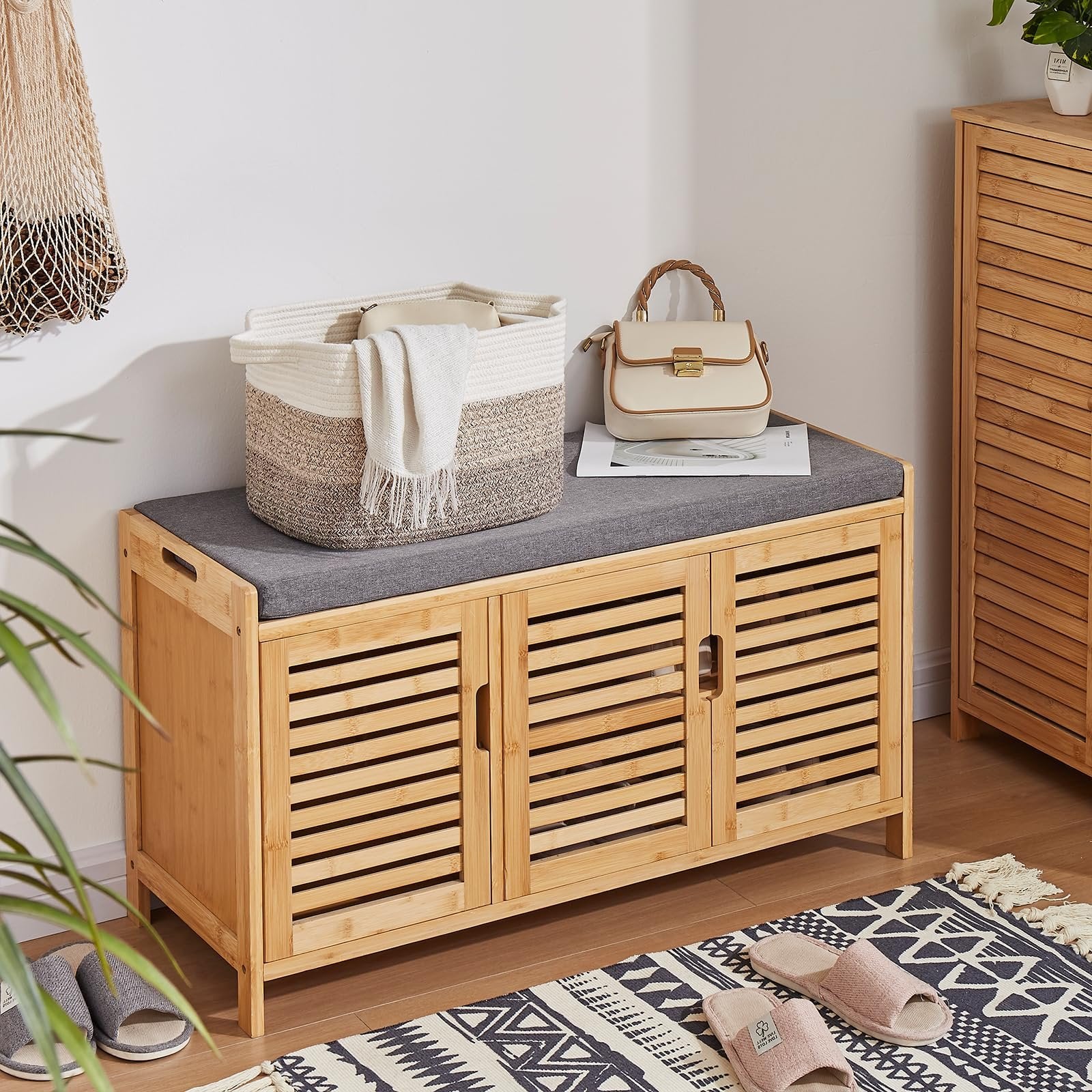 Bamboo shoe cabinet with cushioned top, featuring a woven storage basket and handbag on top, with slippers and rug on floor.