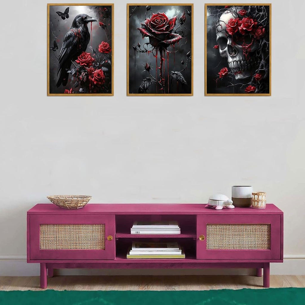 Three framed Halloween diamond art paintings of a raven, a rose, and a skull with red roses, displayed above a pink cabinet.