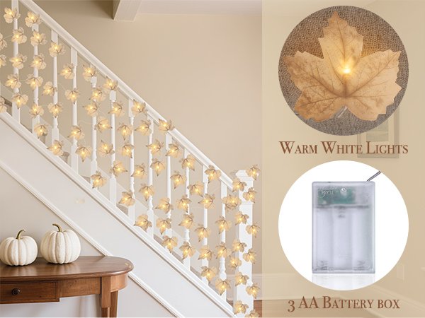 Lighted maple leaf garland draped on a staircase railing with two white pumpkins on a table below