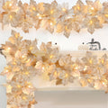 Lighted maple leaf garland draped over a white mantelpiece with small white pumpkins