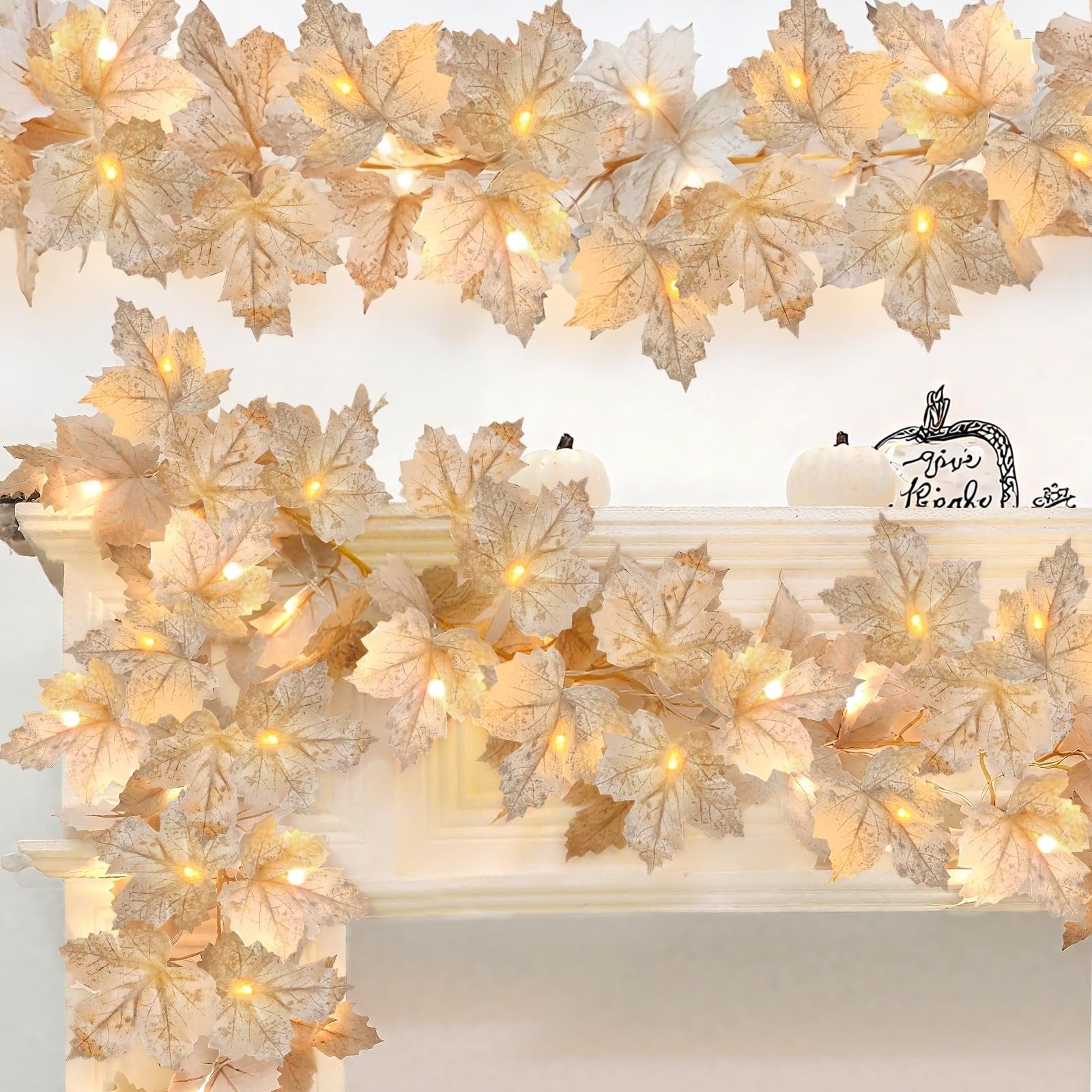 Lighted maple leaf garland draped over a white mantelpiece with small white pumpkins