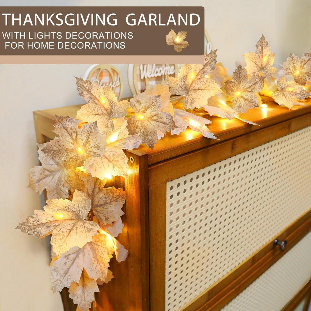 Lighted maple leaf garland draped over a wooden surface with decorative elements in the background.