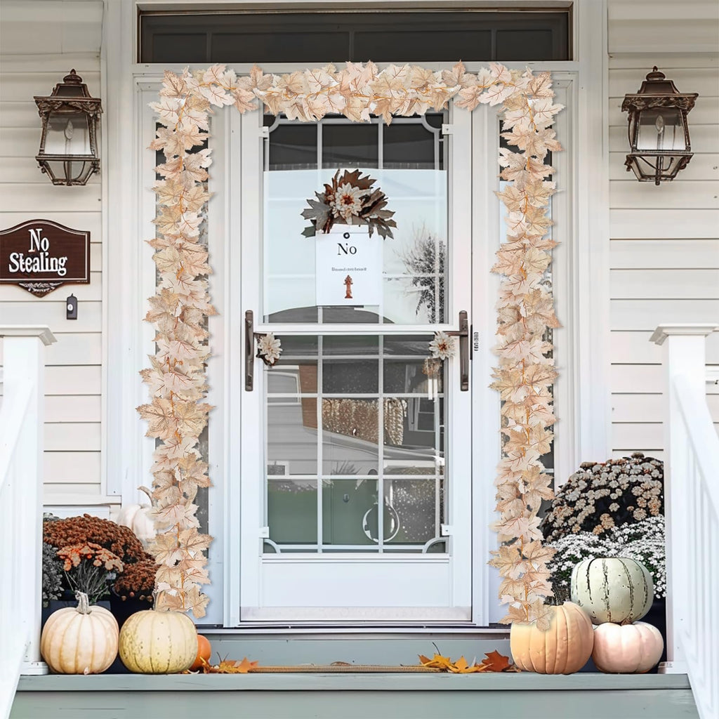 Lighted maple leaf garland draped around a front door with pumpkins and mums on the porch