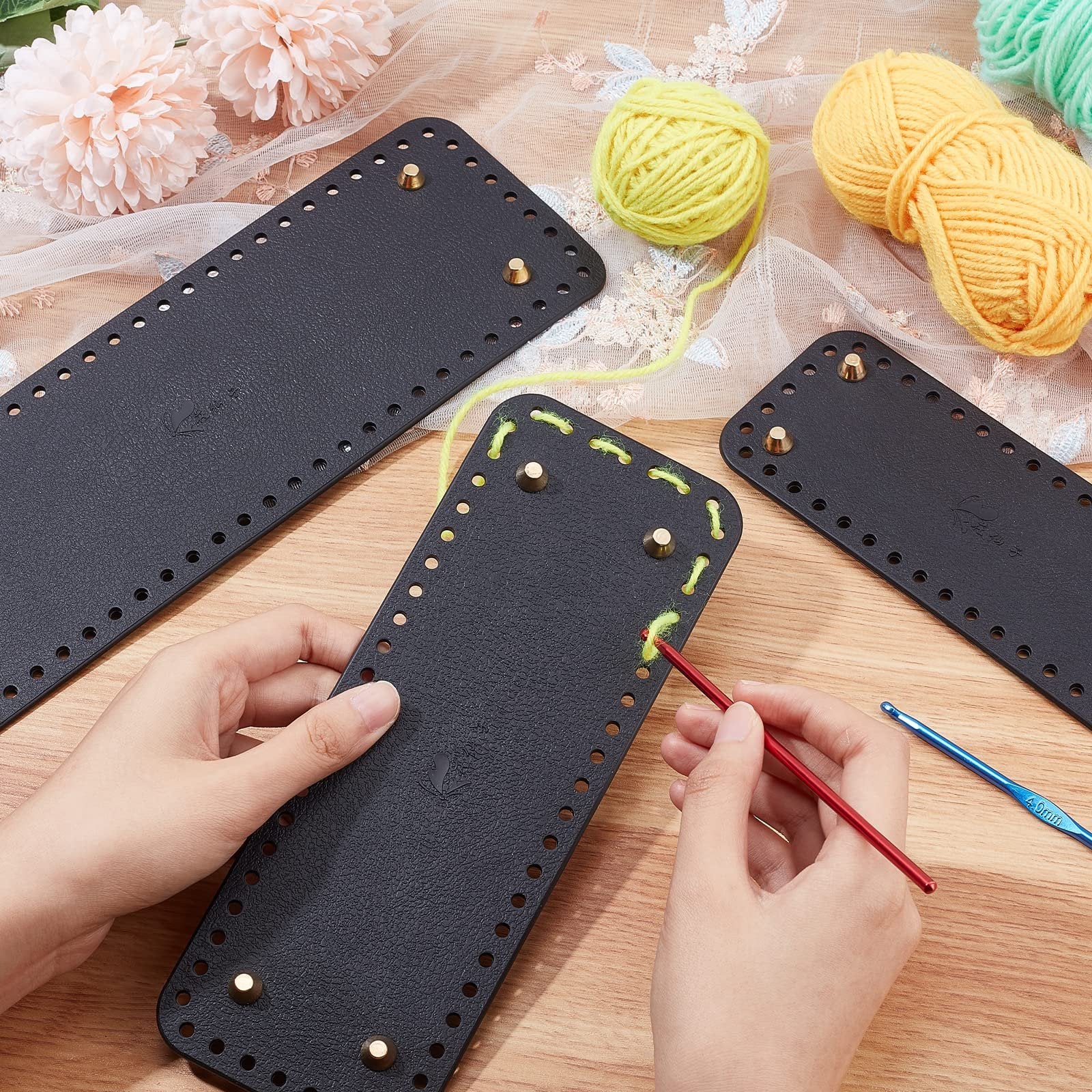 Three black leather purse bottoms with pre-punched holes and brass feet, one being crocheted with yellow yarn and a red hook.