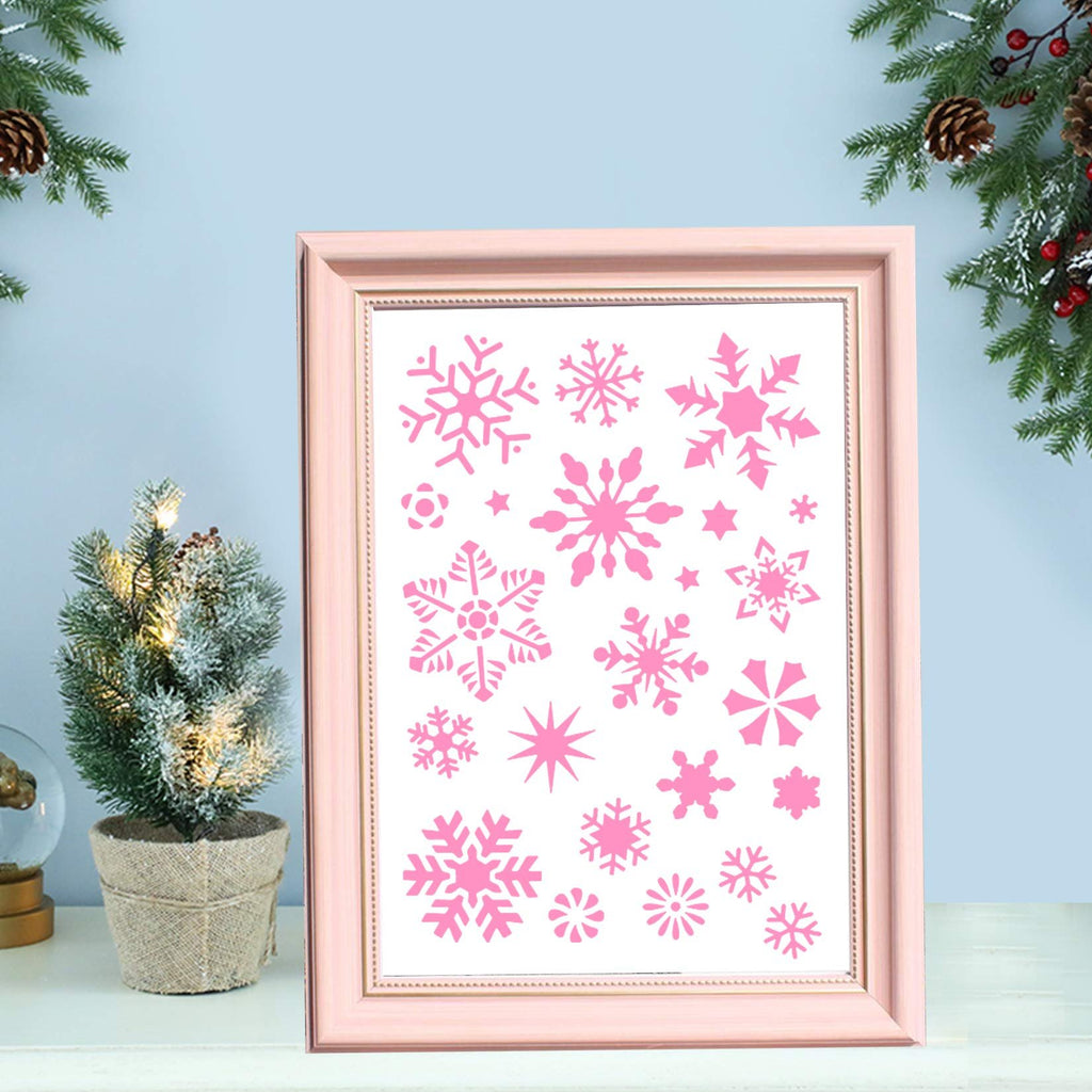 Pink snowflake stencils displayed in a light pink picture frame, with a small decorated Christmas tree and pine branches on either side.