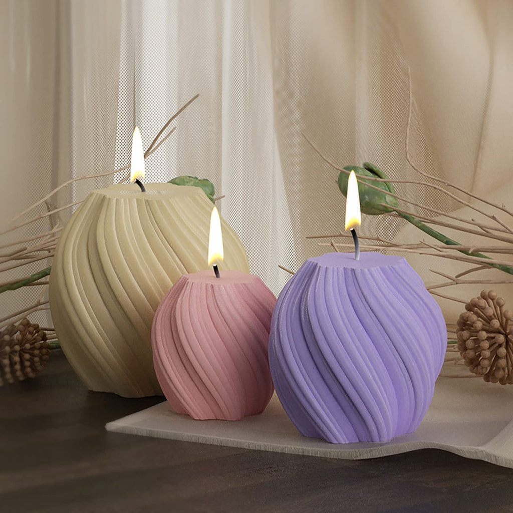 Three lit candles in pastel yellow, pink, and purple, showcasing a twisted wave pattern, arranged on a tray with decorative dried elements.