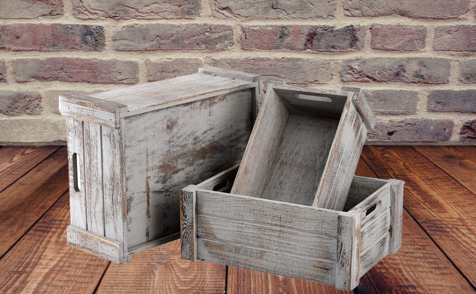 Three rustic white wooden crates with handles stacked and arranged on a wooden floor against a brick wall.