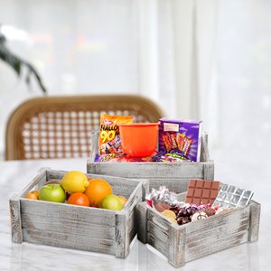 Three rustic wooden crates filled with fruit, candy, and Halloween treats on a marble table.