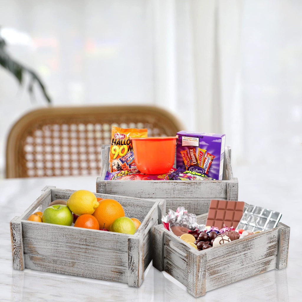 Three rustic wooden crates filled with fruit and candy on a marble surface. The crate in front contains apples, oranges, and lemons. The middle crate holds candy and a Halloween bucket. The back crate is filled with more candy.