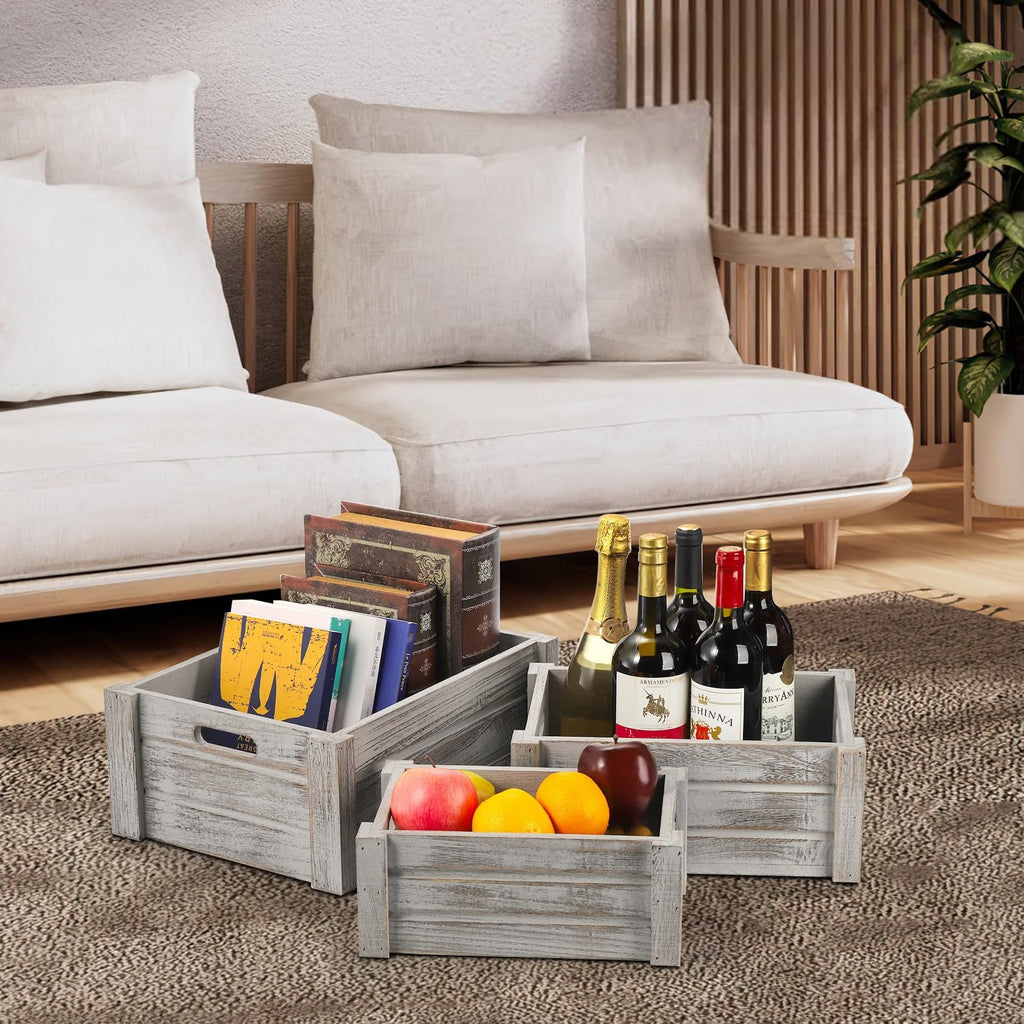 Three rustic wooden crates filled with books, wine bottles, and fruit, arranged on a rug in front of a sofa.