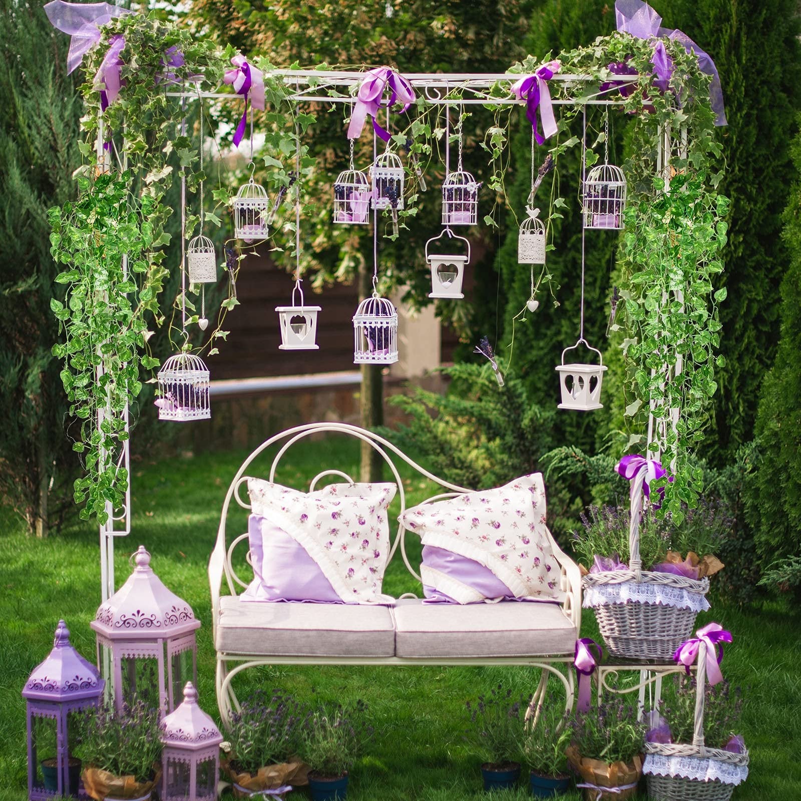 Outdoor garden arch decorated with artificial ivy vines, hanging birdcages, lanterns, and a bench with pillows.