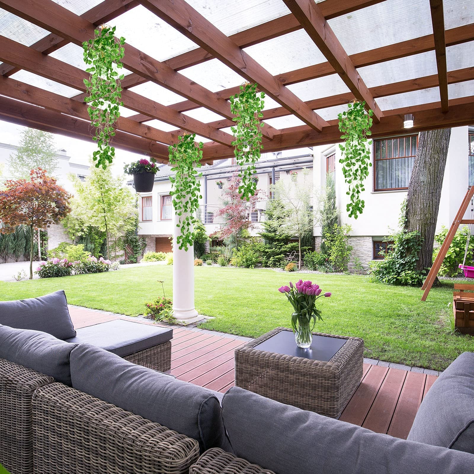 Artificial purple ivy vines with fairy lights hanging from a wooden pergola over a patio with outdoor furniture.