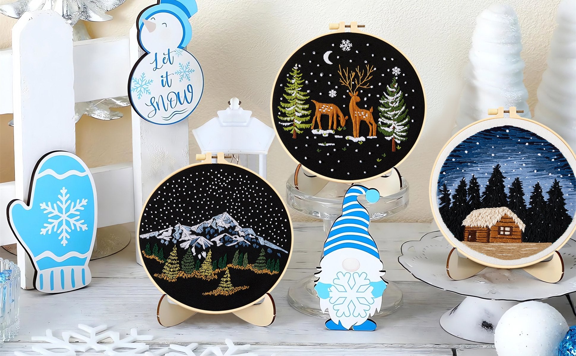 Three embroidered hoops with winter scenes and decorative winter figures on a white surface.
