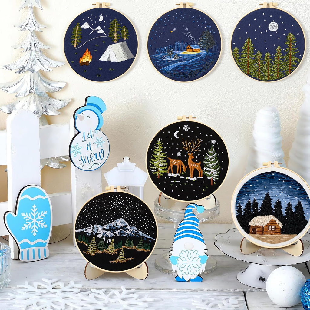 Collection of embroidered hoops with winter scenes and festive decorations on a white surface.