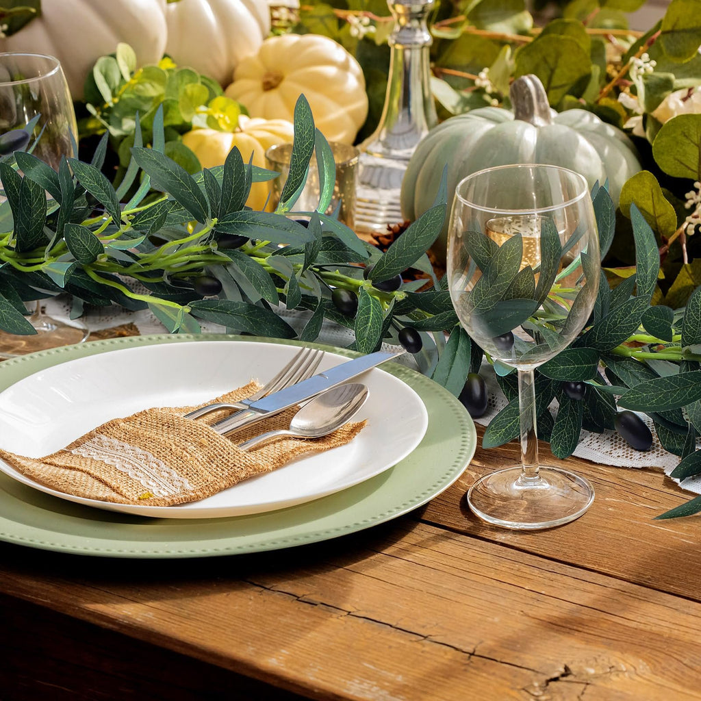 Table setting with artificial olive garland, pumpkins, and wine glass
