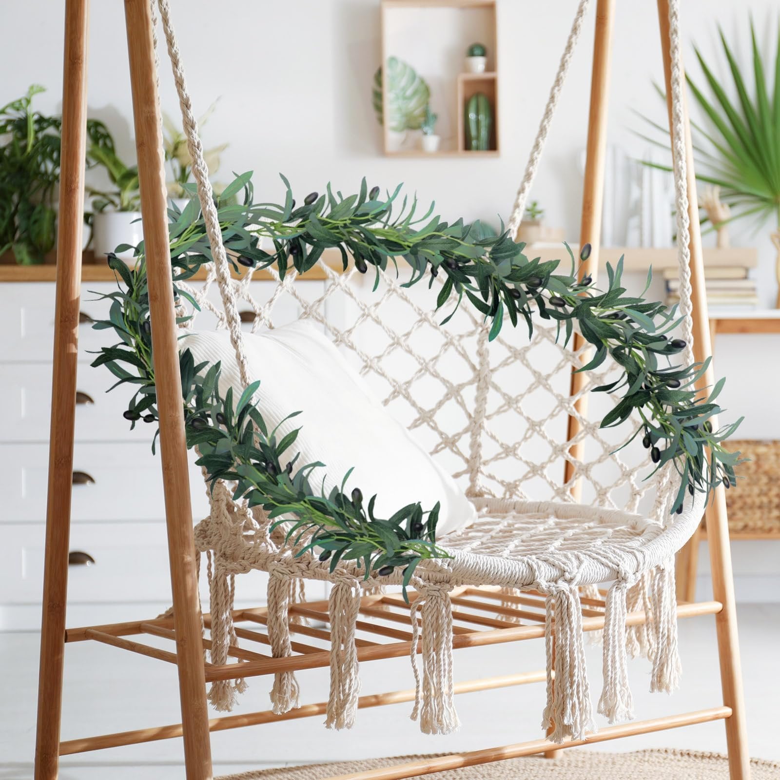 Artificial olive leaf garland with black olives draped over a macrame swing chair with a white pillow