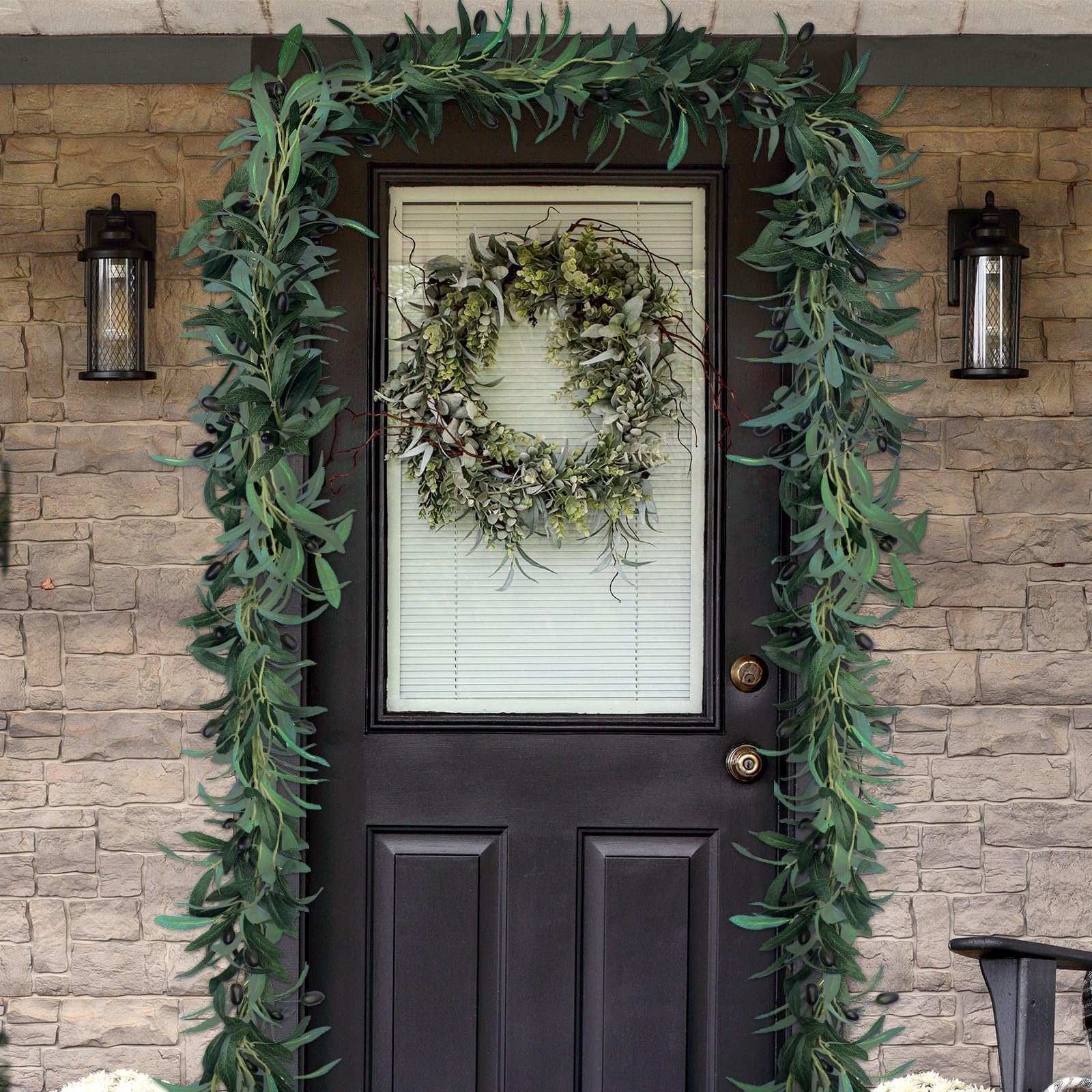Artificial olive leaf garland with black olives draped around a black front door with a wreath on the glass pane.
