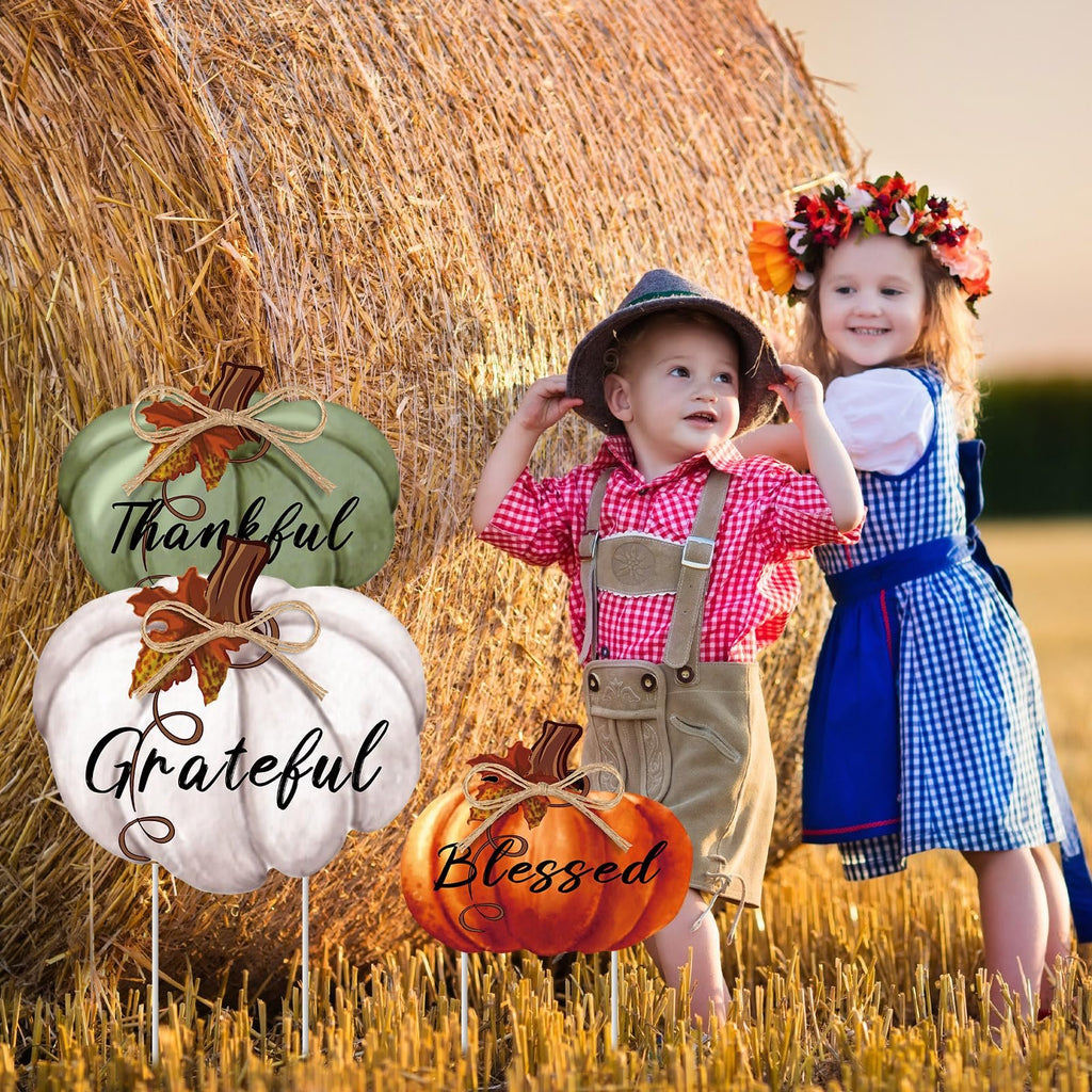 Three Thanksgiving pumpkin yard stakes with words Thankful, Grateful, and Blessed, in a field with two children.