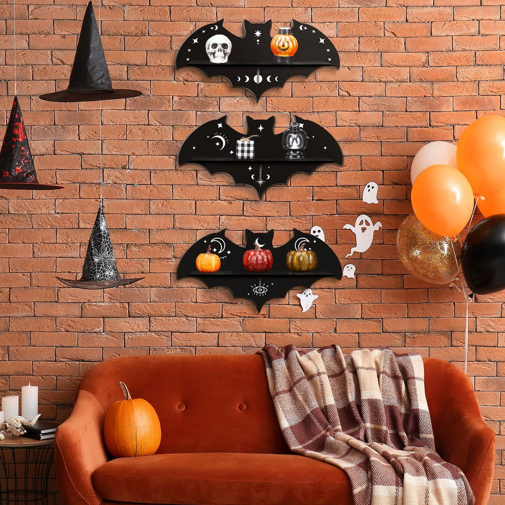 Three black bat-shaped shelves with Halloween decorations displayed on a brick wall above a sofa.