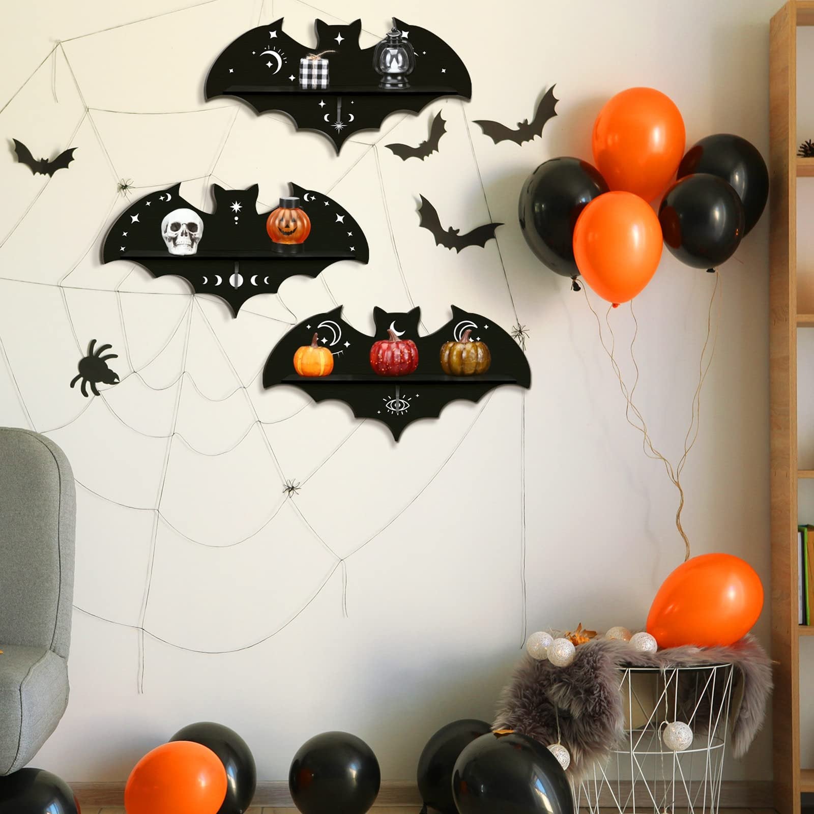 Three black bat-shaped shelves decorated with Halloween motifs, displaying pumpkins and a skull, with balloons and spiderwebs in the background.