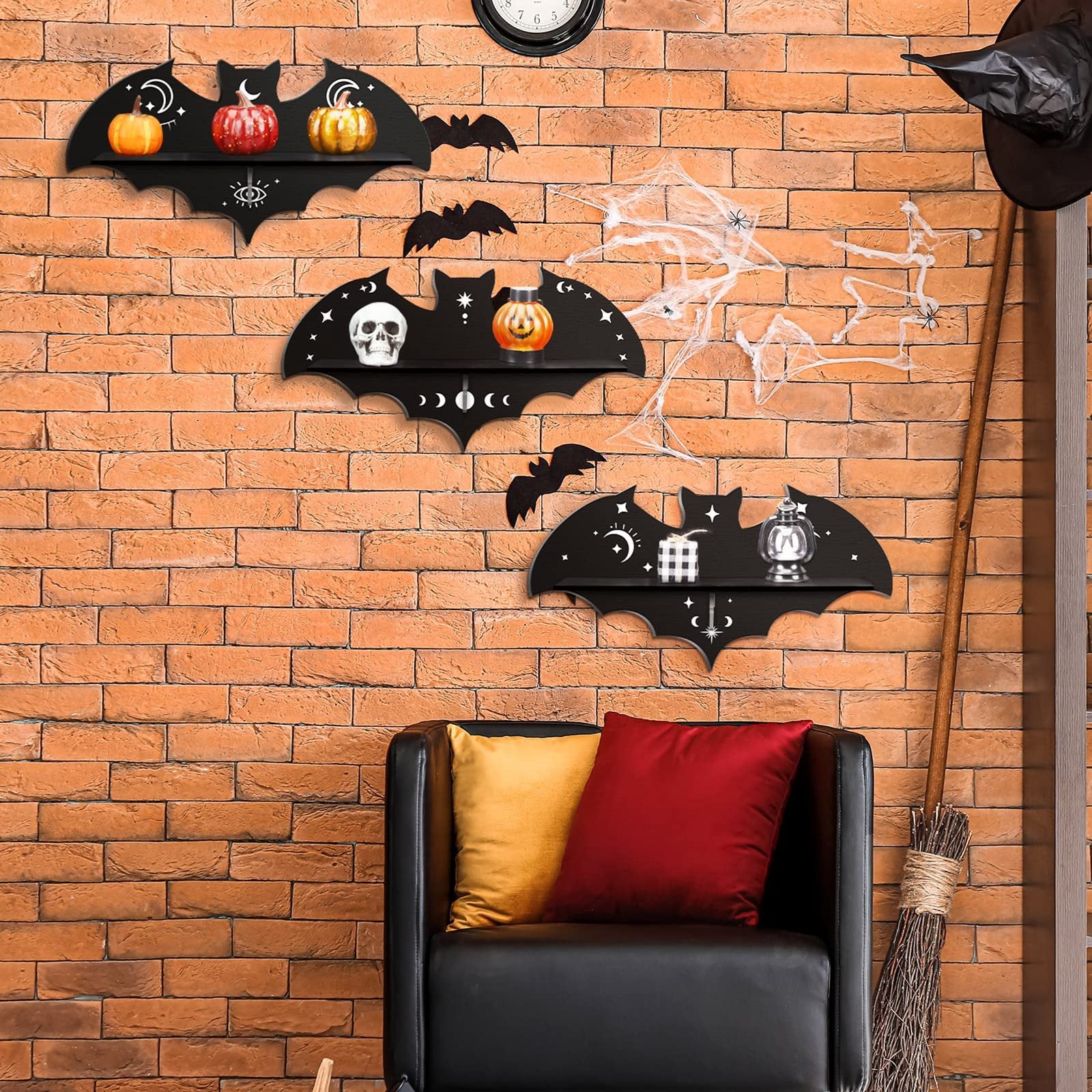Three black bat-shaped shelves with Halloween decorations displayed on a brick wall above a black sofa.