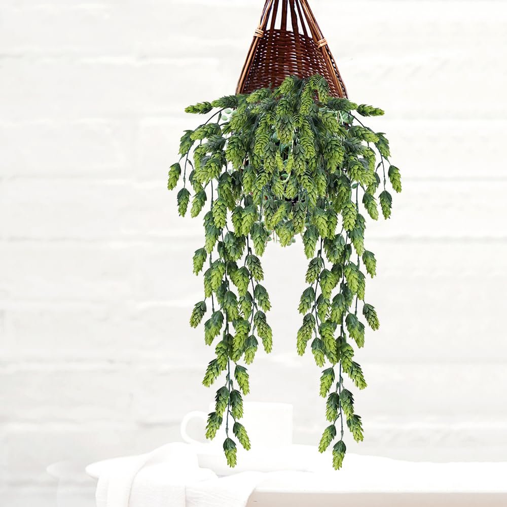 Artificial hops vine hanging from a woven basket, with a white mug and cloth in the foreground.