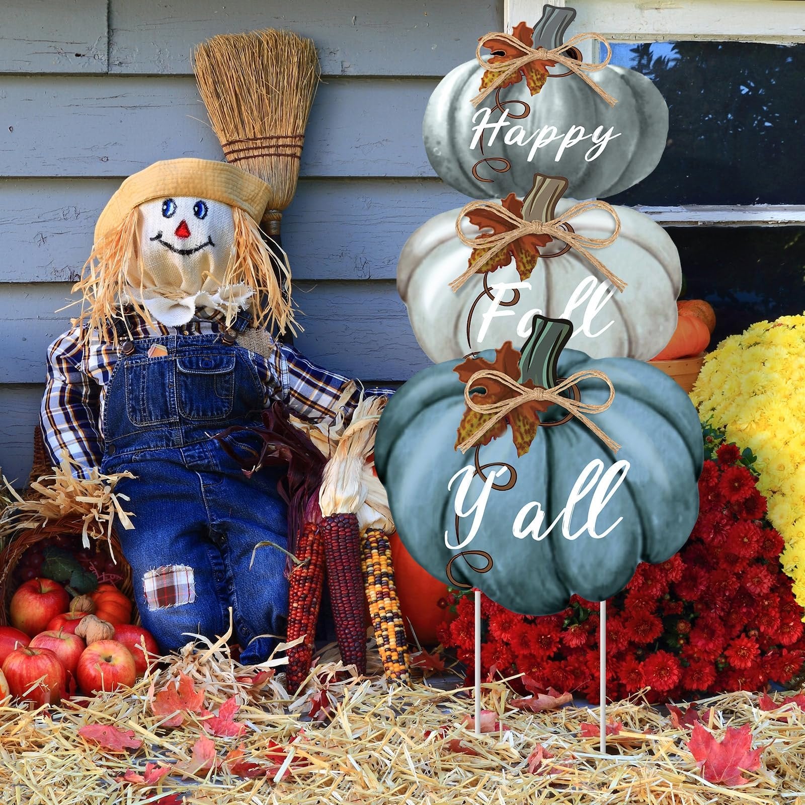 Stackable blue and white pumpkins with 'Happy Fall Y'all' text, next to a scarecrow and fall flowers.