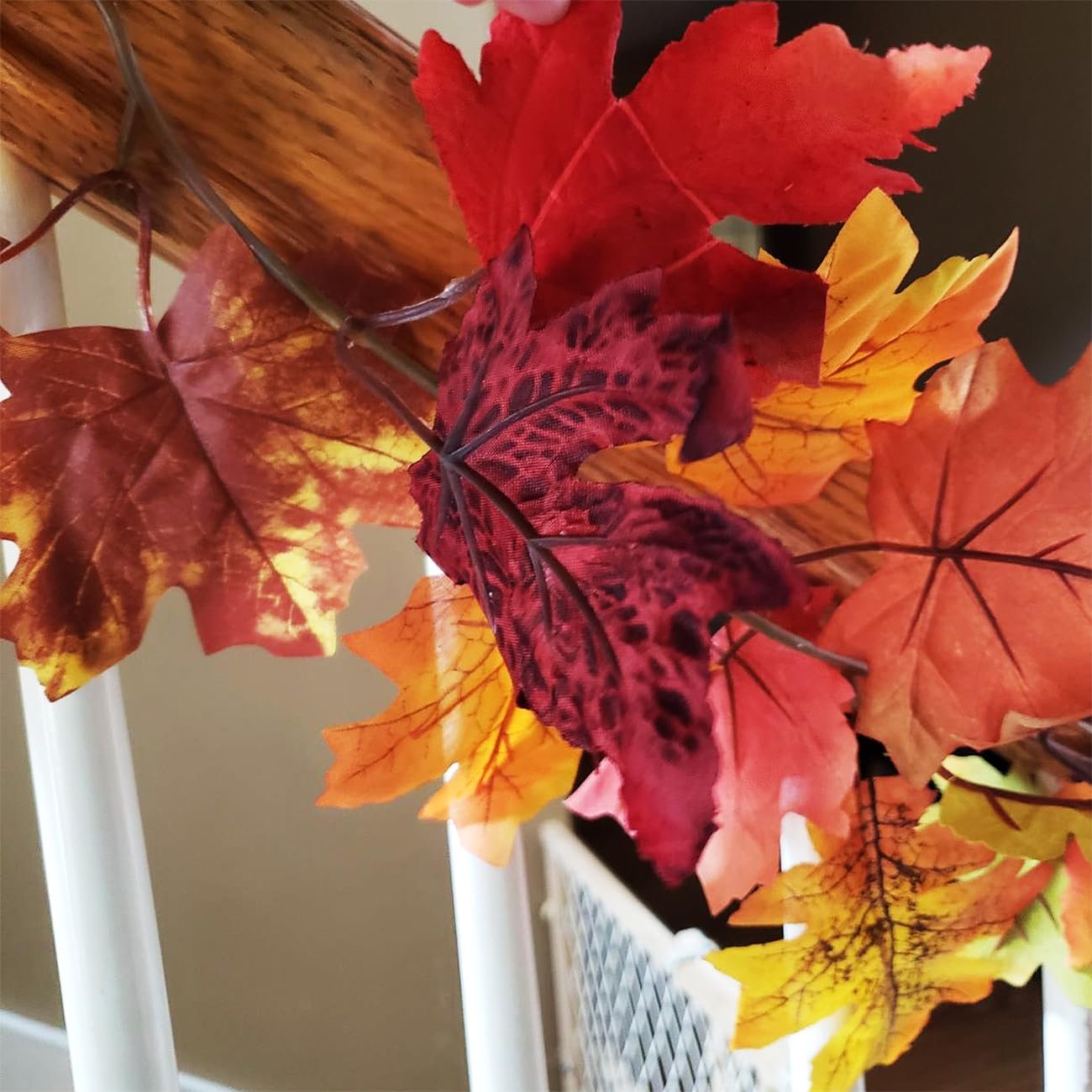 Close-up of a faux fall maple leaf garland with red, orange, and yellow leaves draped over a wooden railing.