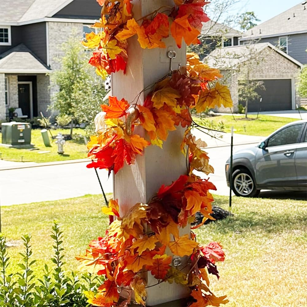 Autumn maple leaf garland wrapped around a white post in a suburban yard with houses and a car in the background.