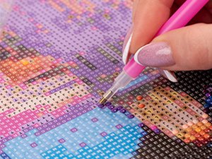 Close-up of a hand using a pink tool to place a diamond onto a 5D diamond art kit with a dwarf design.