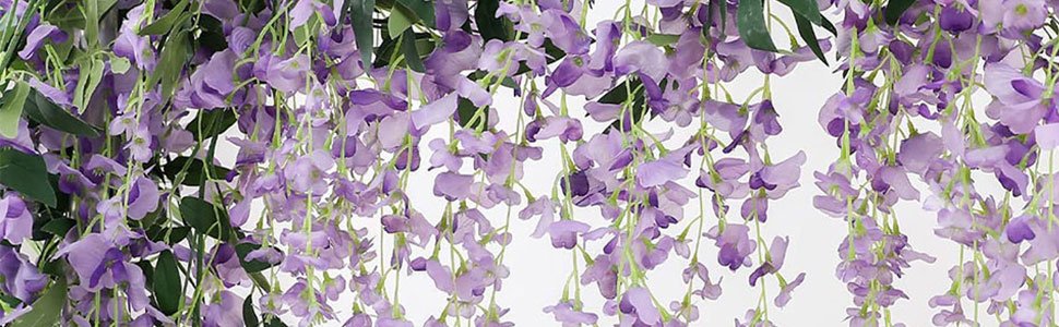 Close-up of cascading purple artificial wisteria flowers with green leaves against a white background.