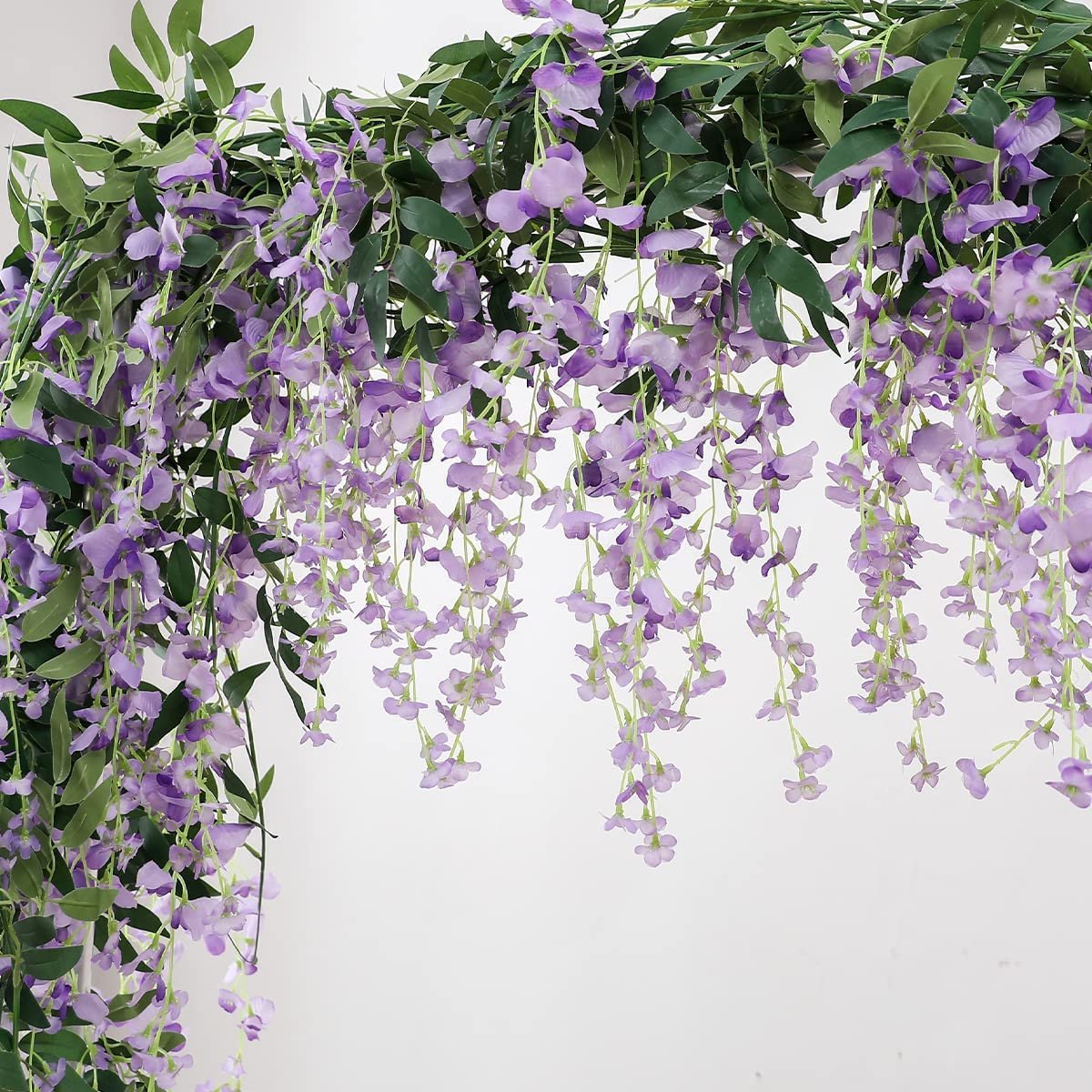 Artificial purple wisteria garland with green leaves cascading against a white background.