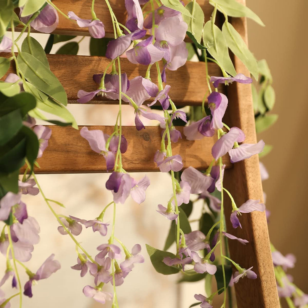 Purple artificial wisteria flower garlands with green leaves draped over a wooden ladder.