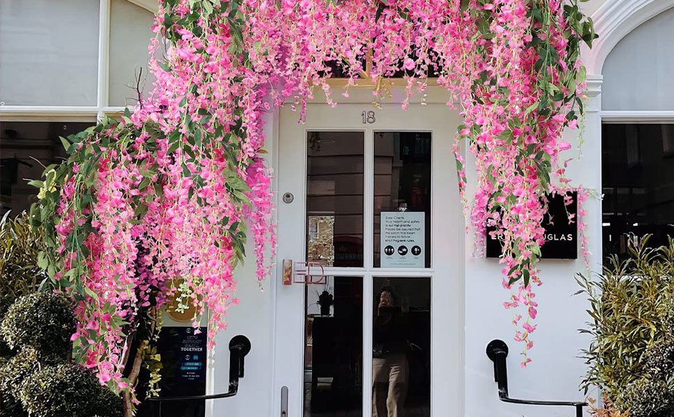Artificial fuchsia wisteria garlands draped over a white doorway and archway, with green leaves and pink flowers.