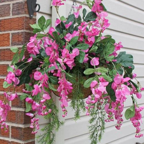 Hanging basket filled with artificial fuchsia wisteria flowers and green leaves, shown outdoors.